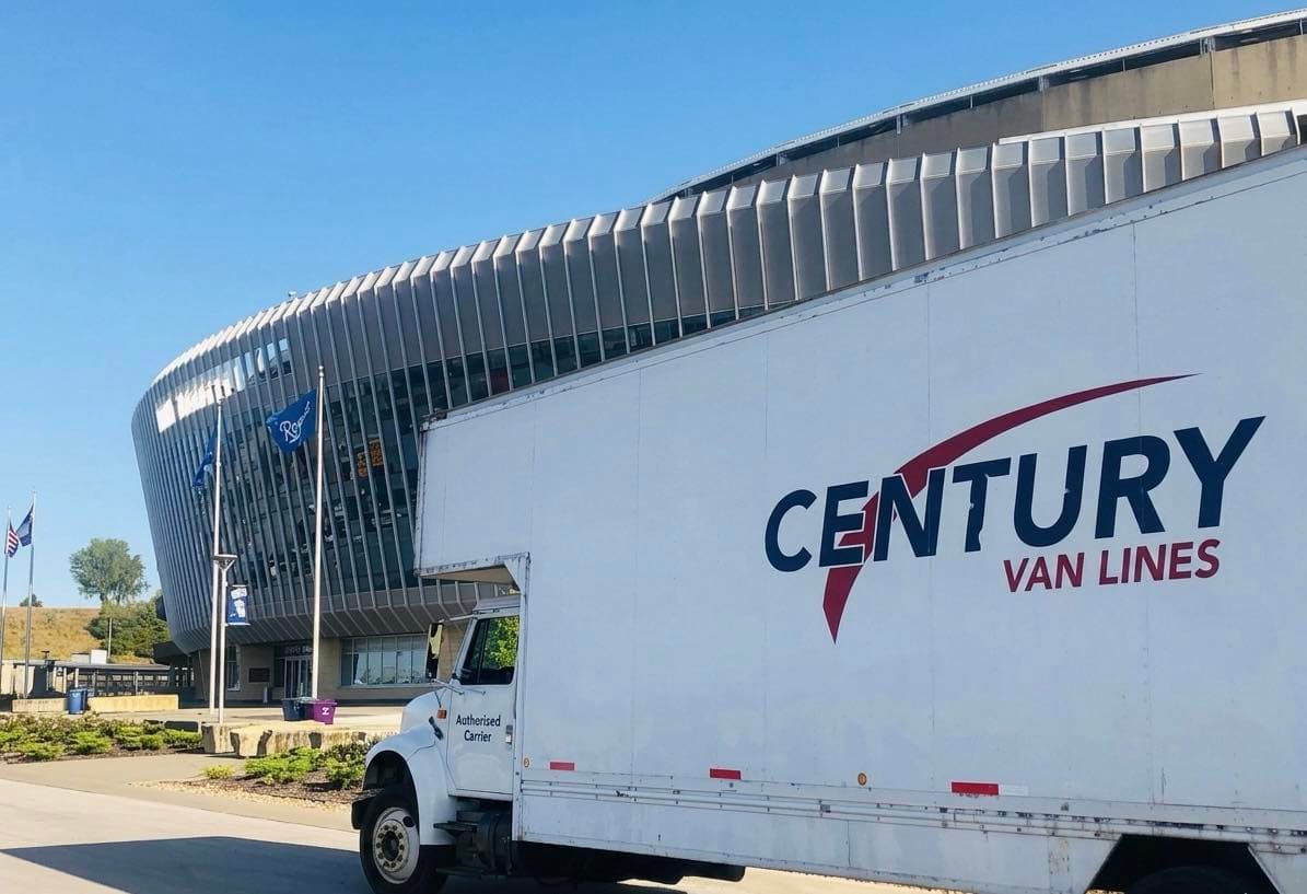 White Century Van Lines truck parked in front of a large, modern stadium.