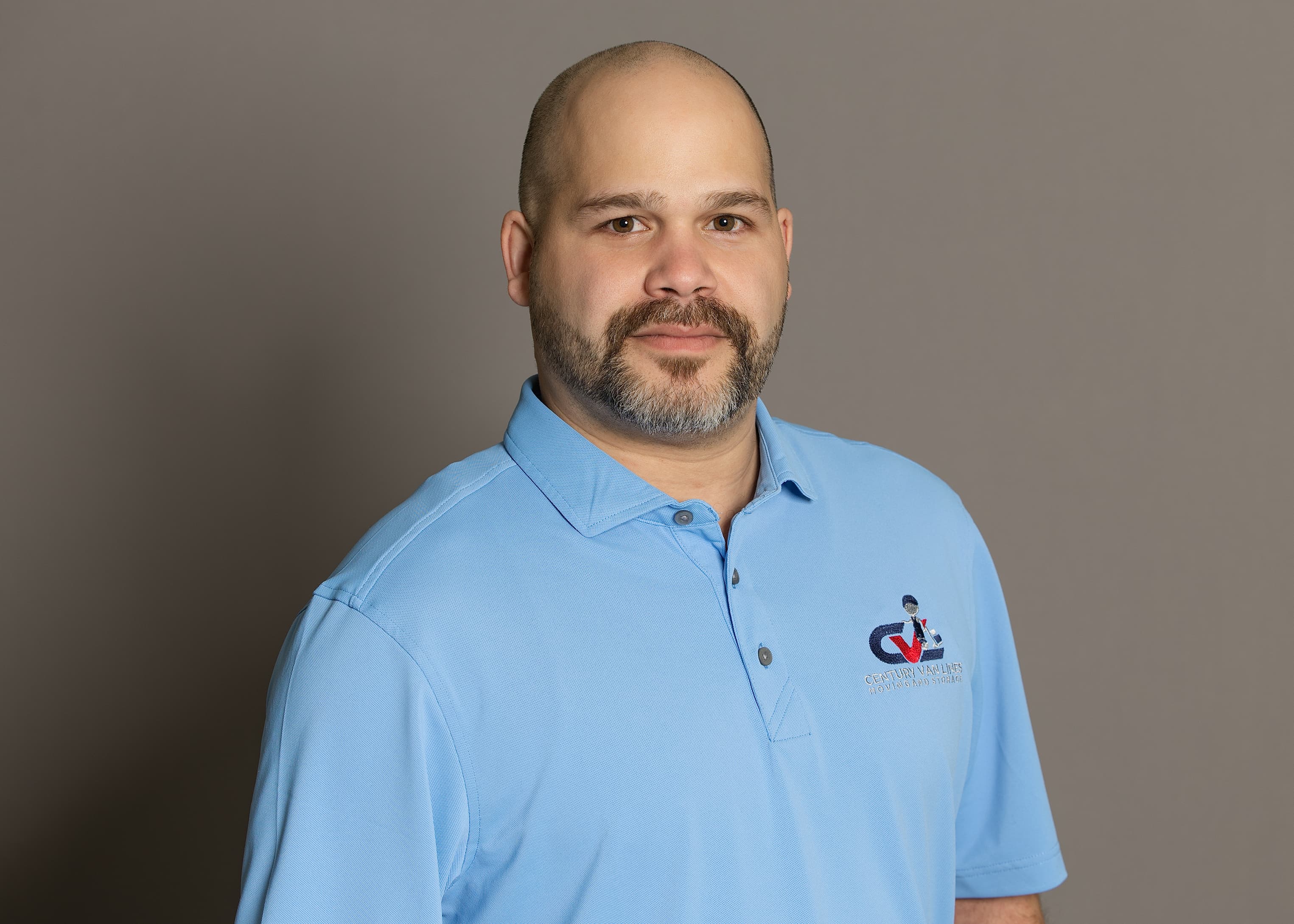 Bald man with a goatee wearing a light blue Century Van Lines polo shirt.