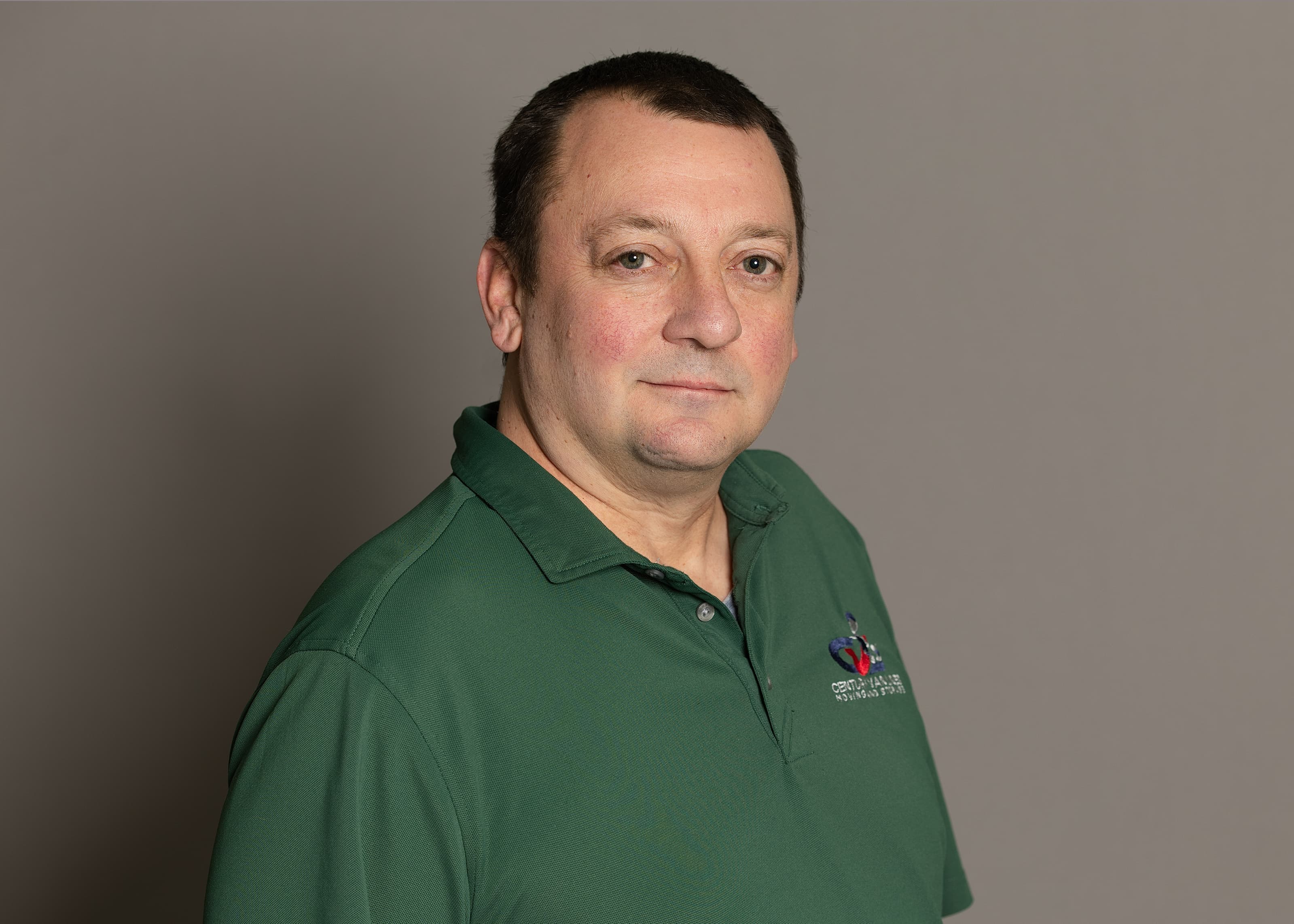 Middle-aged man with short dark hair wearing a green polo shirt against a gray background.