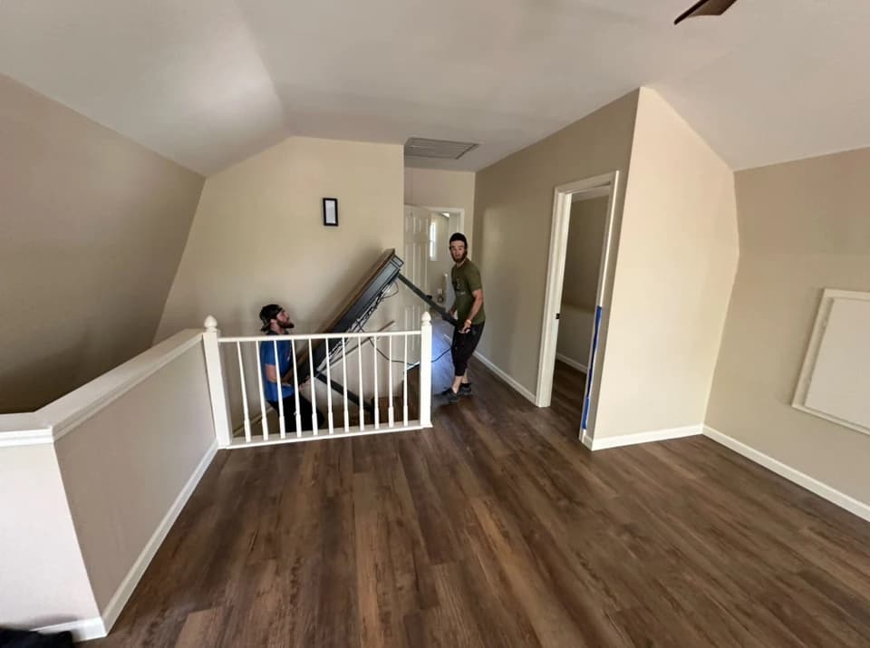 Two men maneuver a large, flat object up a staircase into a room.