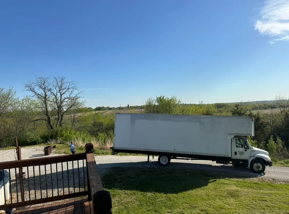 White box truck parked on a gravel driveway beside a wooden deck under a clear sky.